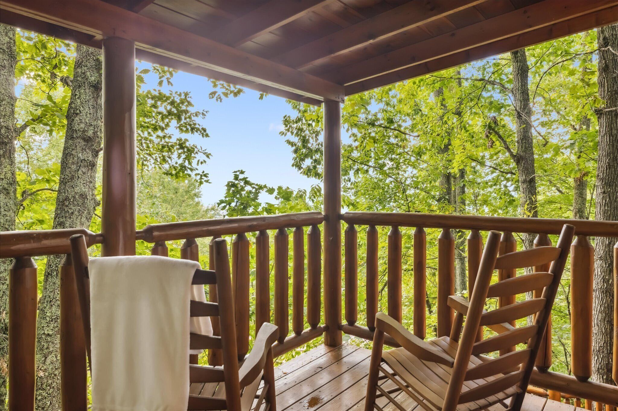 A wooden deck with a railing, two wooden chairs, and a white towel hanging on the railing.