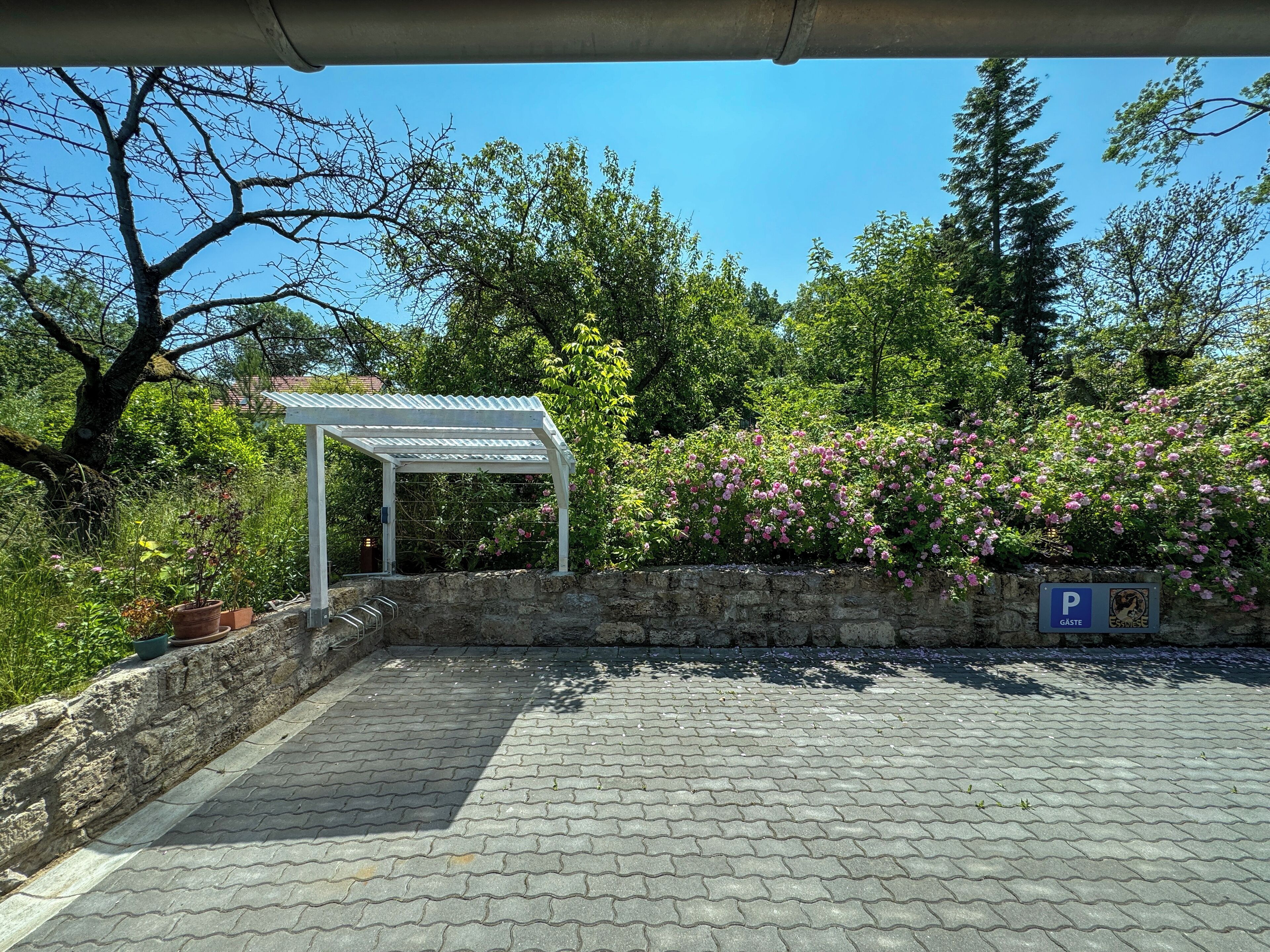A covered parking area with a stone wall and a pergola.