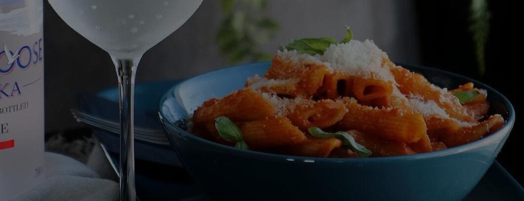 Un plato de pasta con queso rallado y una copa de vino blanco.
