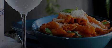 A bowl of pasta with grated cheese and a glass of white wine.