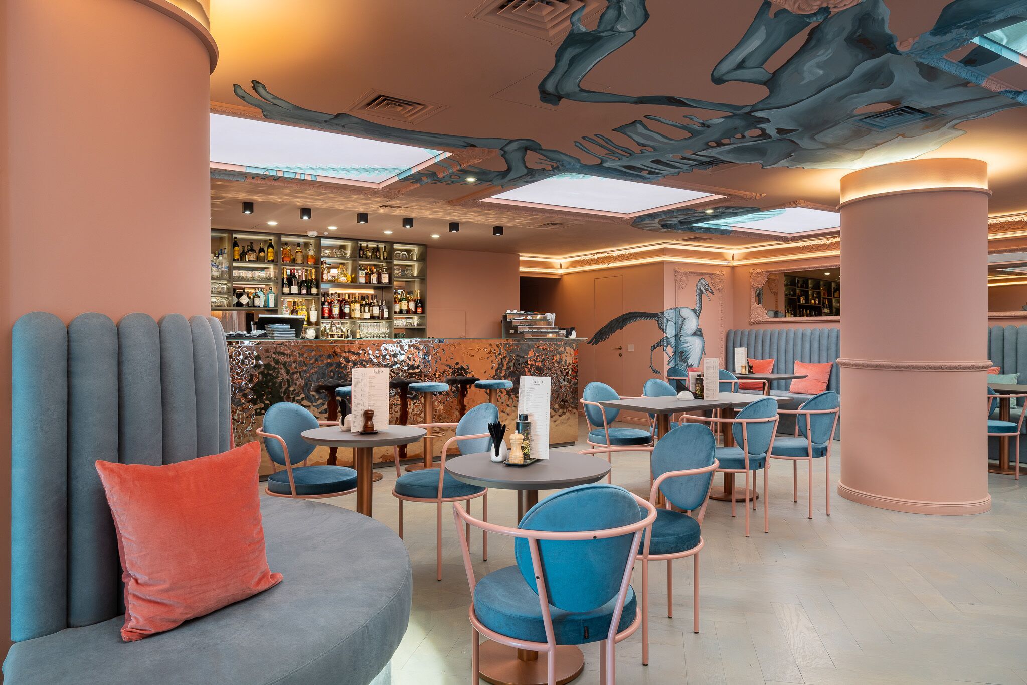 A restaurant with round tables, blue chairs, and a bar area in the background.
