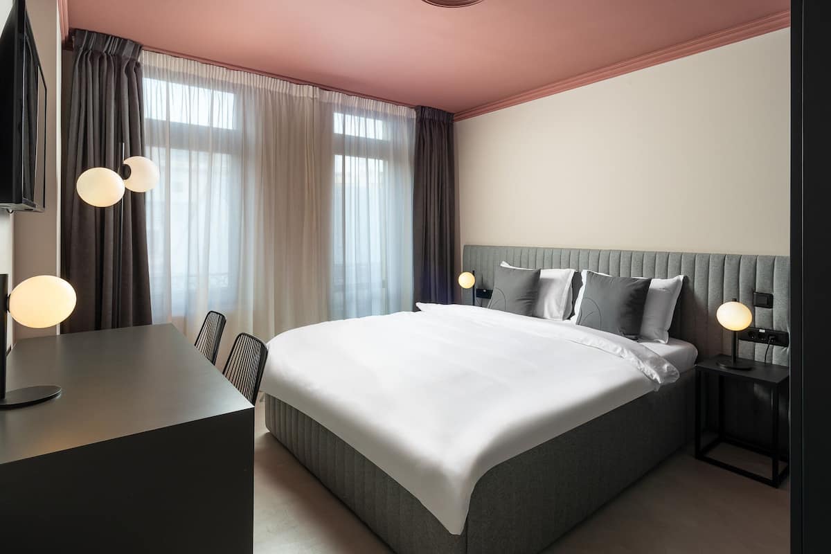 A modern hotel room with a large bed, bedside tables, a desk, and a TV.