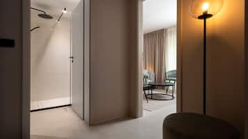 A modern hotel room with a shower, a dining area with a table and chairs, and a standing lamp.
