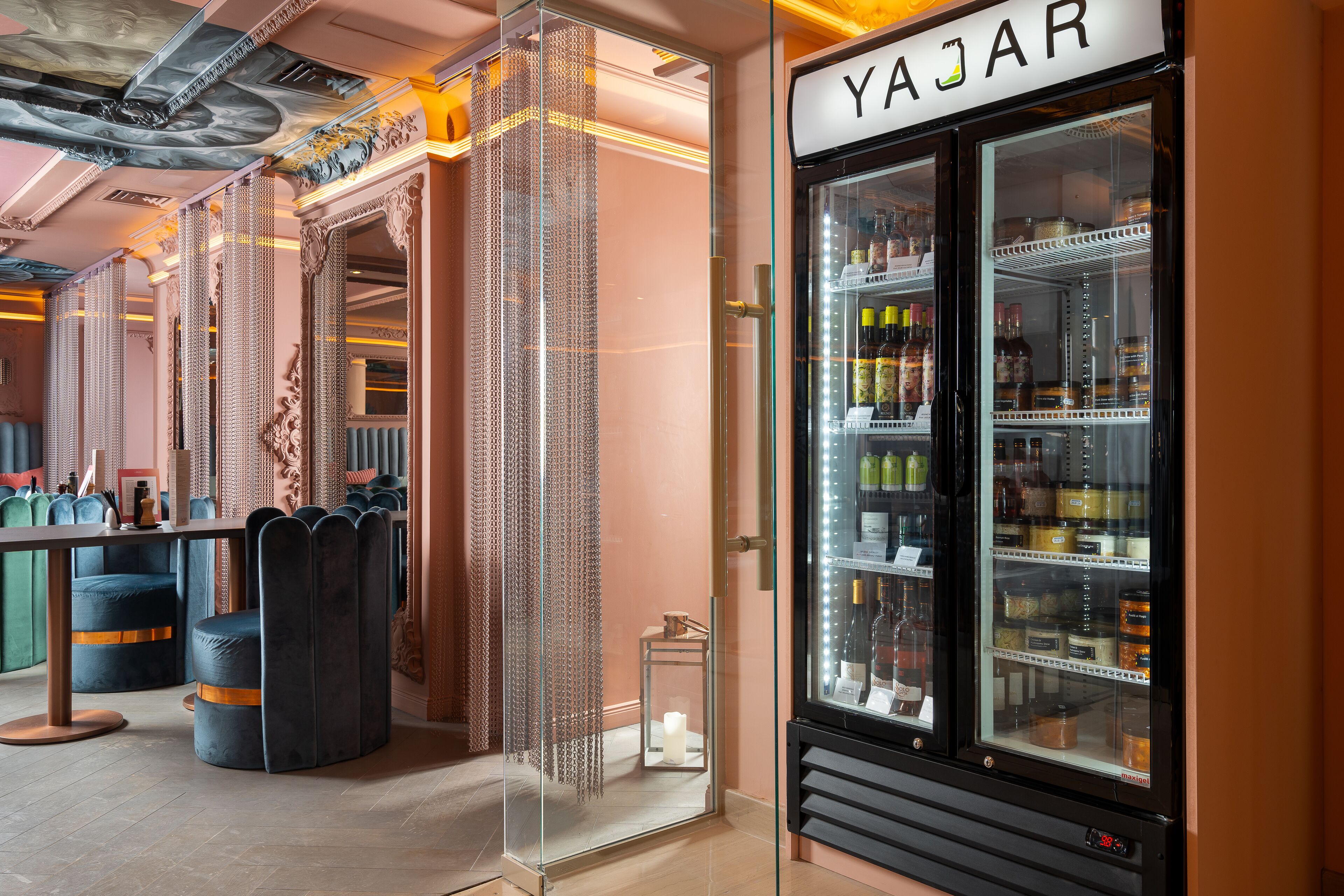 A modern interior with a Yajarl refrigerator stocked with beverages, a seating area with cushioned chairs, and a decorative glass partition.