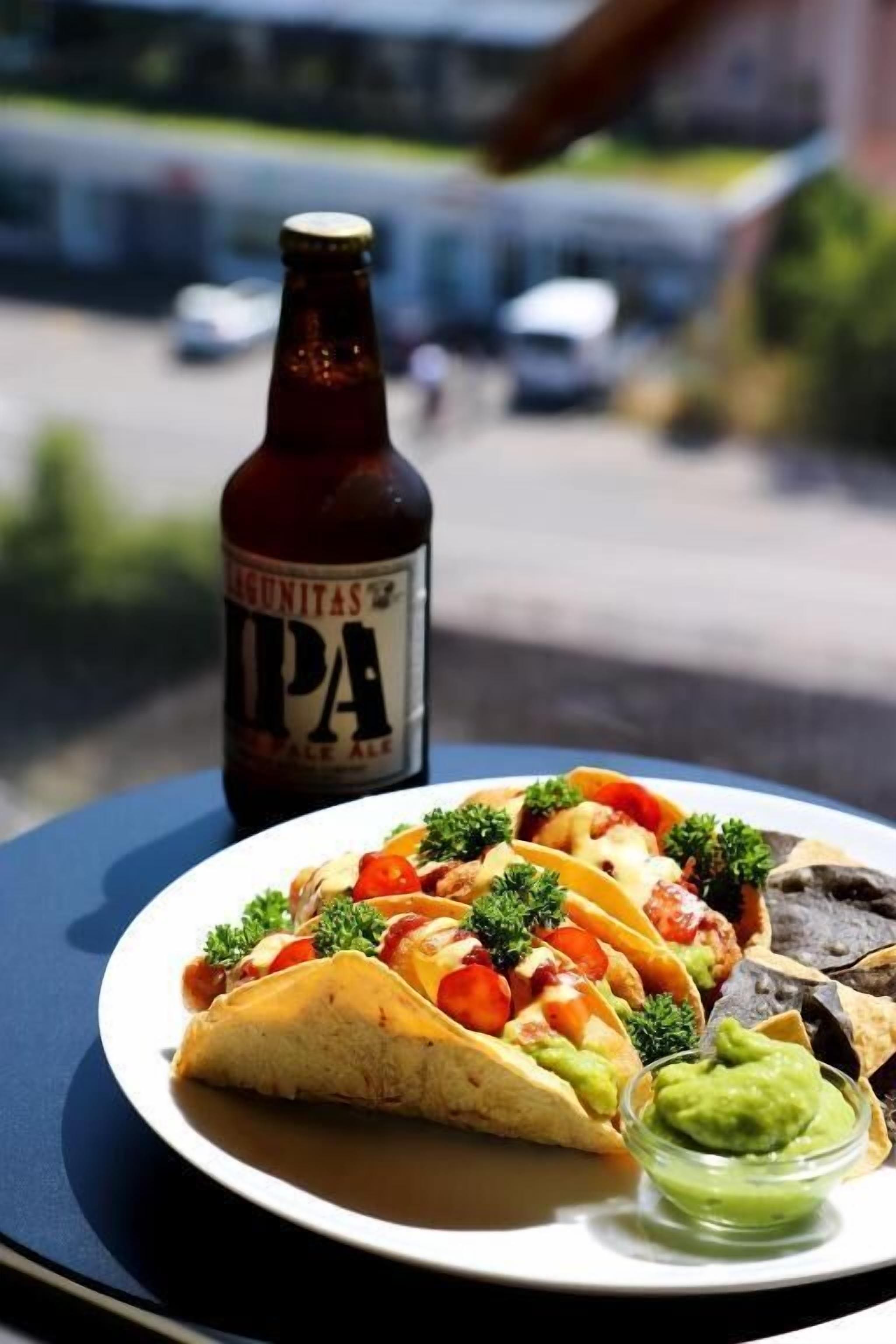 A plate of tacos with guacamole and a bottle of Lagunitas IPA beer on a table.