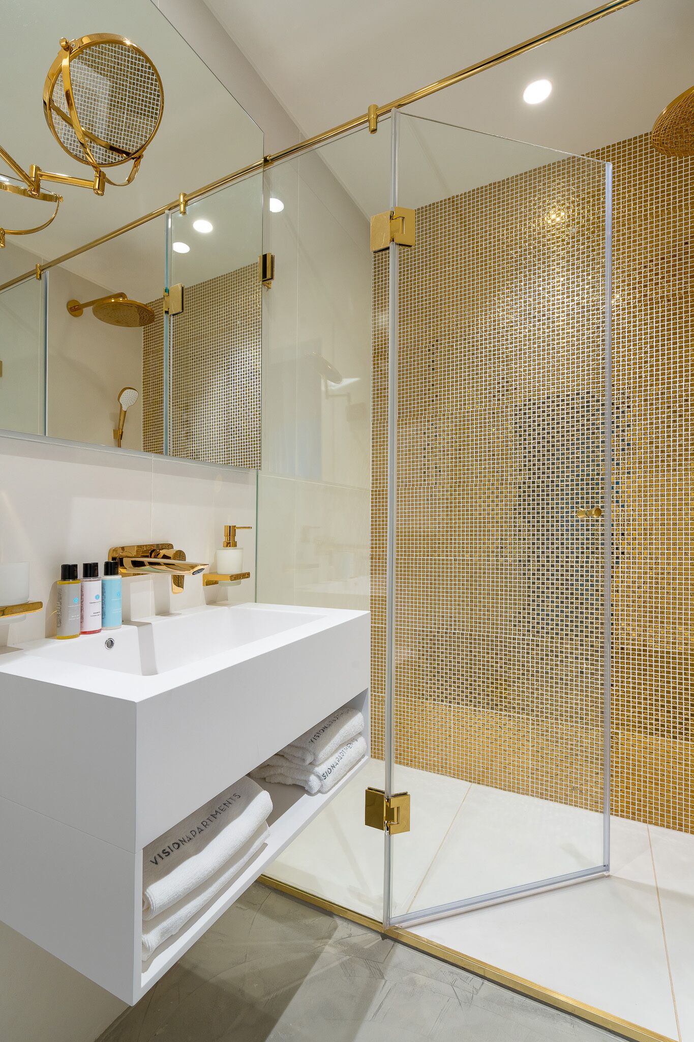 Een moderne badkamer met een douchecabine van glas, een wit wastafelmeubel met gouden details en een grote spiegel.