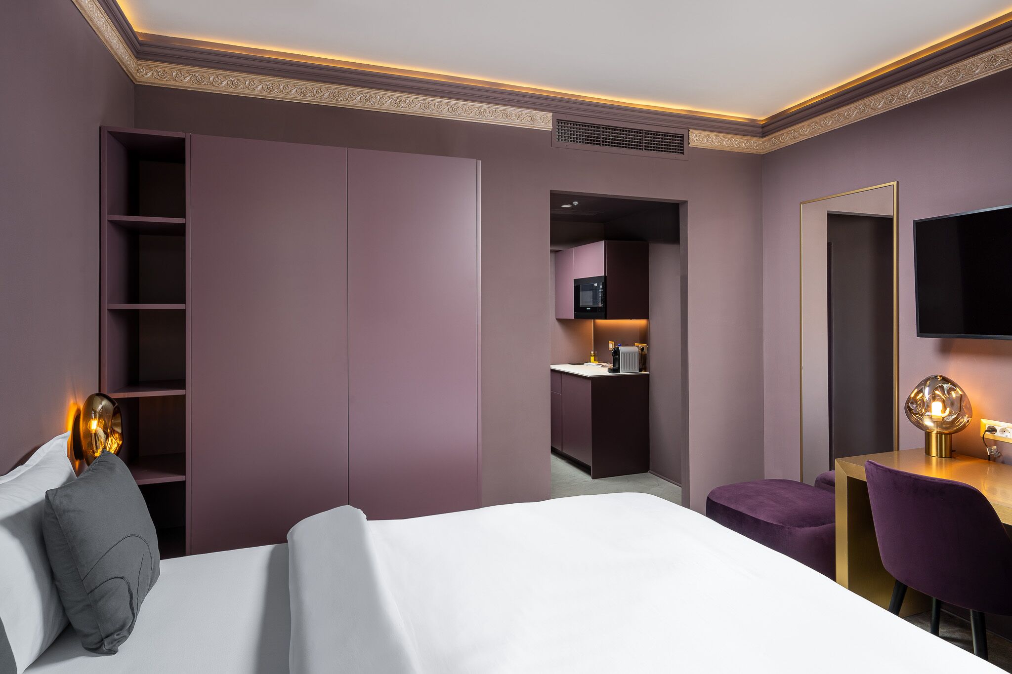 A modern hotel room with a bed, a desk, a chair, and a television.