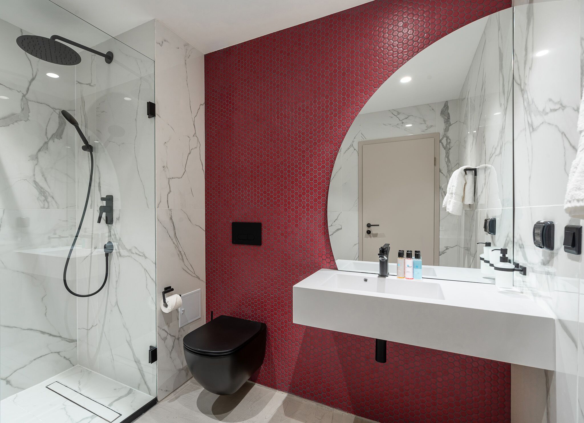 Un baño moderno con ducha de mármol blanco, inodoro negro y pared texturizada de color rojo.