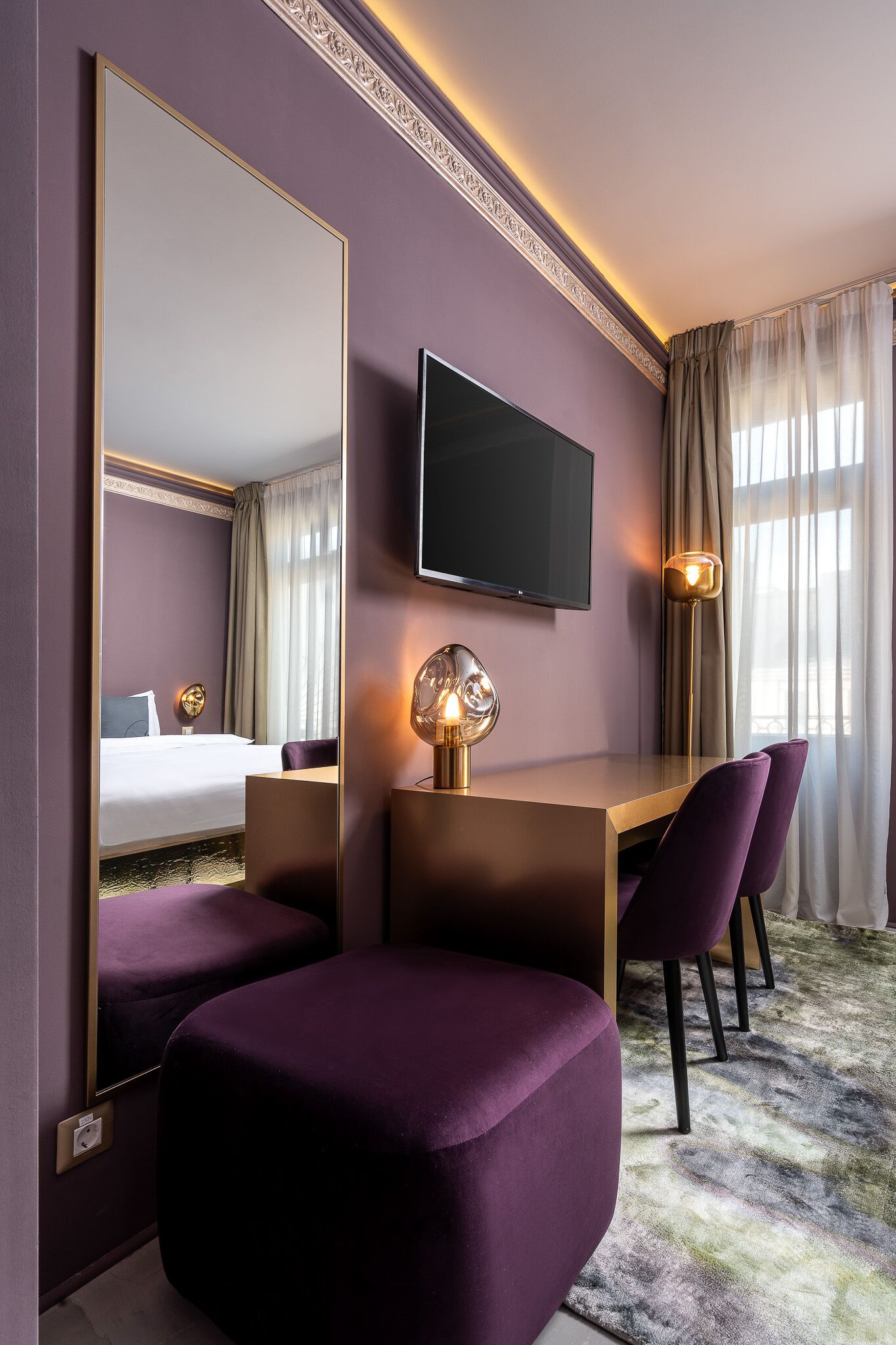 A modern hotel room with a large bed, a desk with two chairs, a flat-screen TV, and a large mirror.