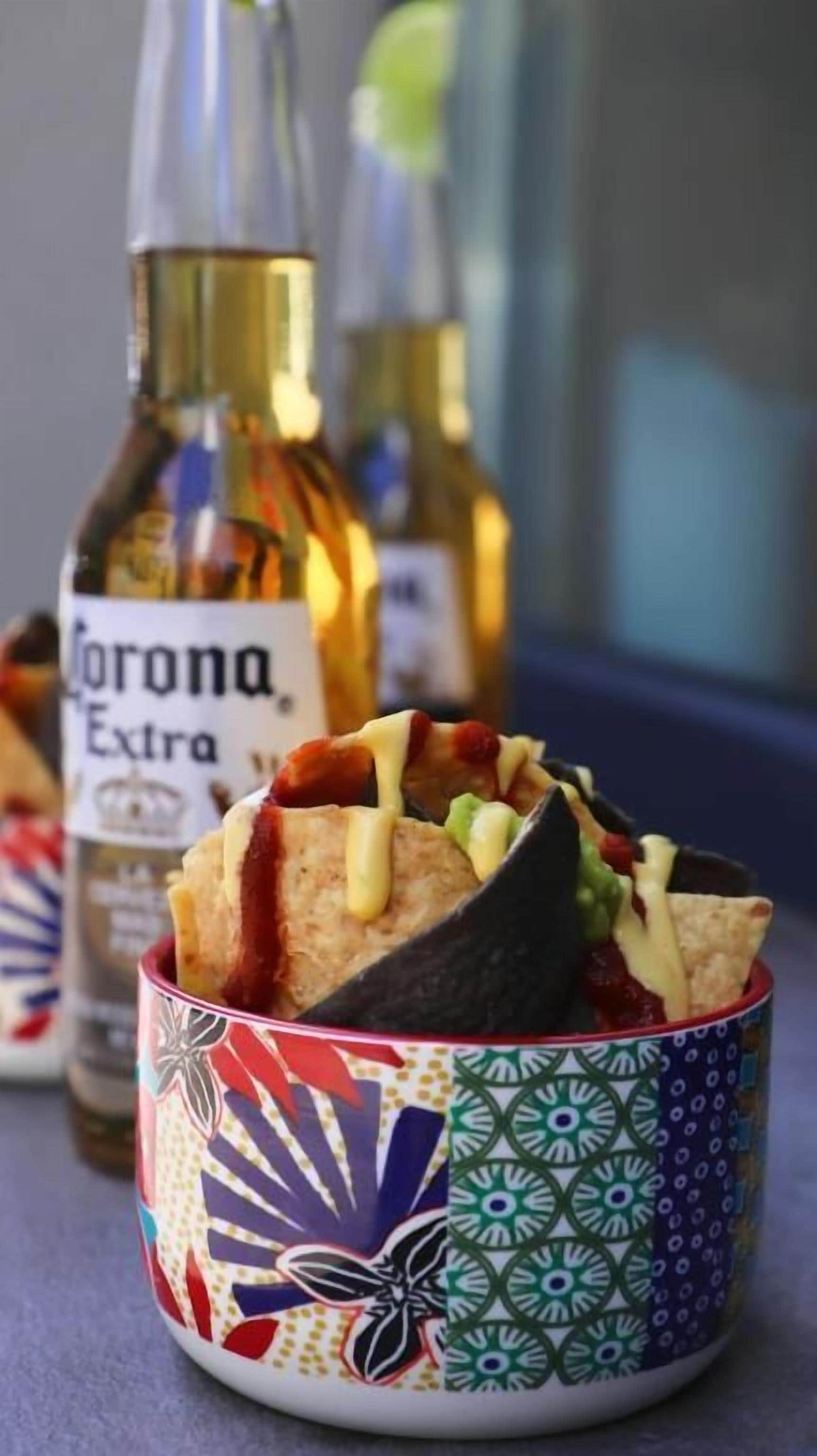 Uma tigela colorida com nachos e, ao fundo, uma garrafa de Corona Extra.