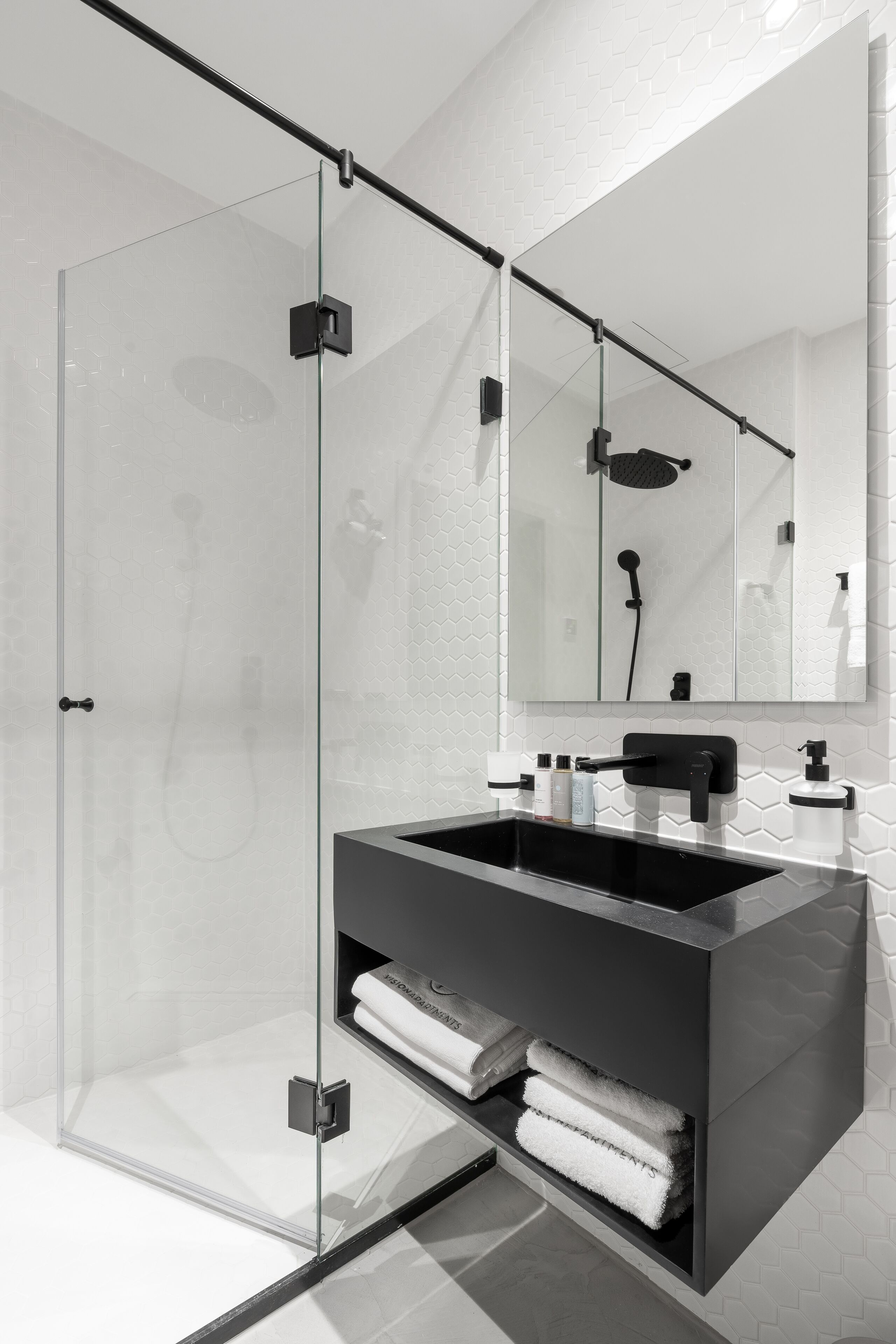 A modern bathroom with a glass-enclosed shower, a black vanity with a mirror, and a white tiled wall.