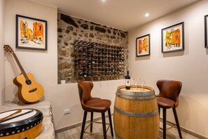 Ein Zimmer mit einer Steinwand, einem Weinregal, zwei Stühlen, einer Gitarre und einem Fass.
