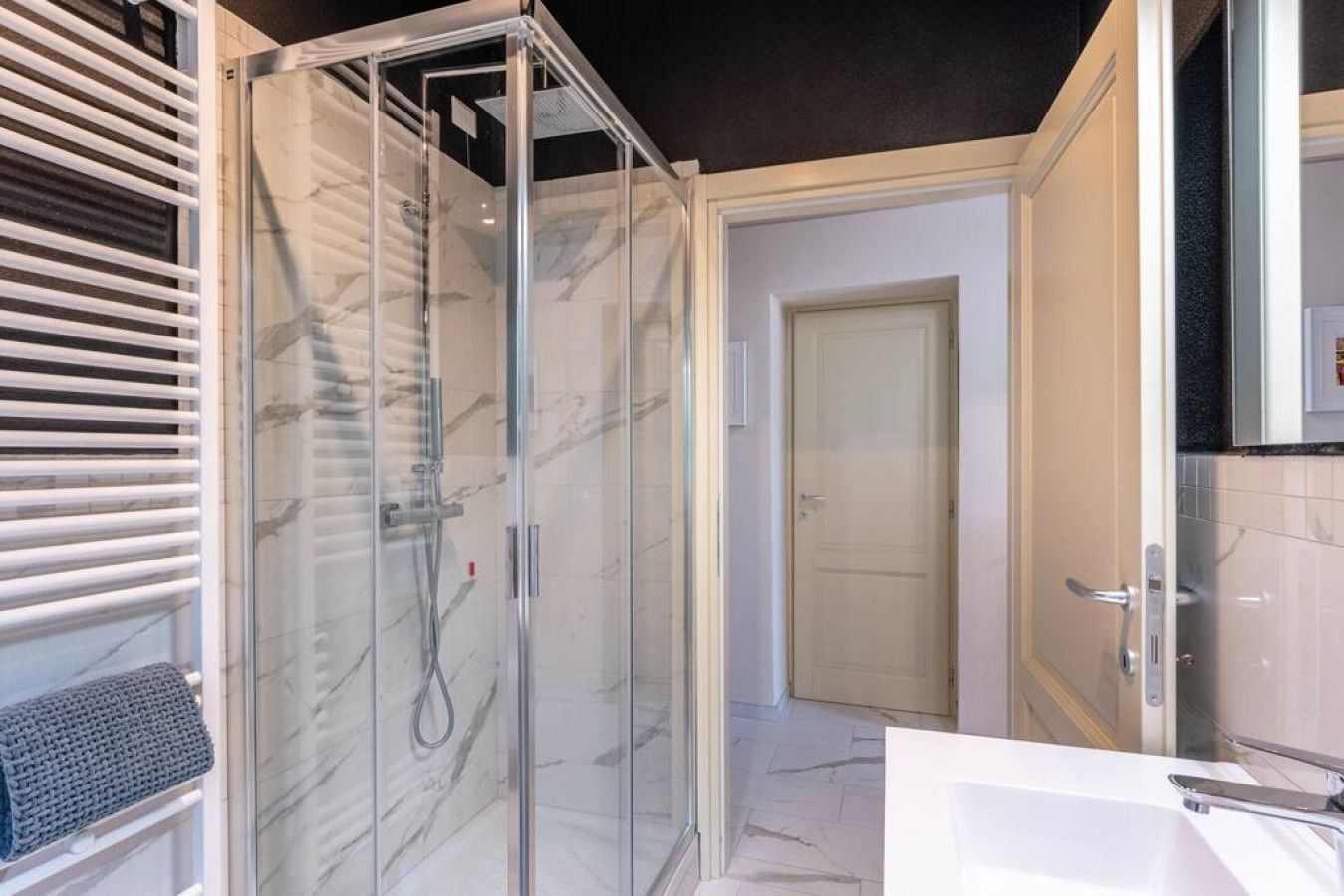 Un bagno moderno con doccia vetrata, una vasca da bagno bianca e una porta che dà su un'altra stanza.