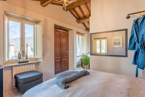 A bedroom with a bed, a window, a door, a radiator, a plant, and a robe on a rack.