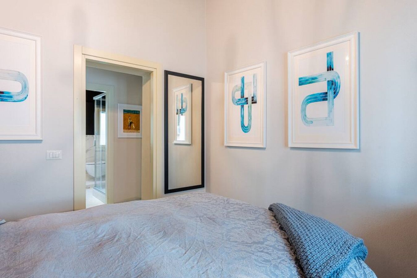 A bedroom with a bed, a door, and three framed artworks on the wall.