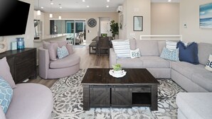 Un salon moderne doté d’un grand téléviseur à écran plat, d’une table basse en bois foncé et d’un canapé gris agrémenté de coussins décoratifs.