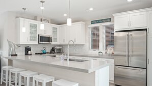 Una cocina moderna con armarios blancos, un refrigerador de acero inoxidable, horno empotrado y una isla grande con taburetes de bar.