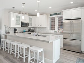 A modern kitchen with white cabinetry, a stainless steel refrigerator, a built-in oven, and a large island with bar stools.
