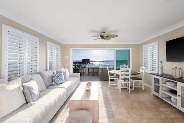 Spacious and bright beachfront living space with coastal decor, plenty of seating and outdoor panoramic ocean views.