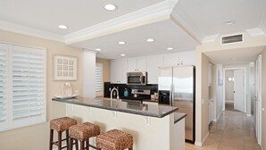 A kitchen with a central island, bar stools, a microwave, a refrigerator, and a sink.