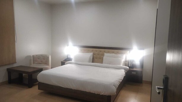 Una habitación de hotel con una cama grande, dos mesitas de noche, una silla y una puerta.