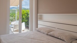 Ein Schlafzimmer mit Bett, einer Schiebetür zu einer Sitzgelegenheit im Freien und Blick ins Grüne.