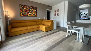Ein modernes Wohnzimmer mit einer Eckcouch, einem Esstisch mit Stühlen und einem farbenfrohen abstrakten Gemälde an der Wand.