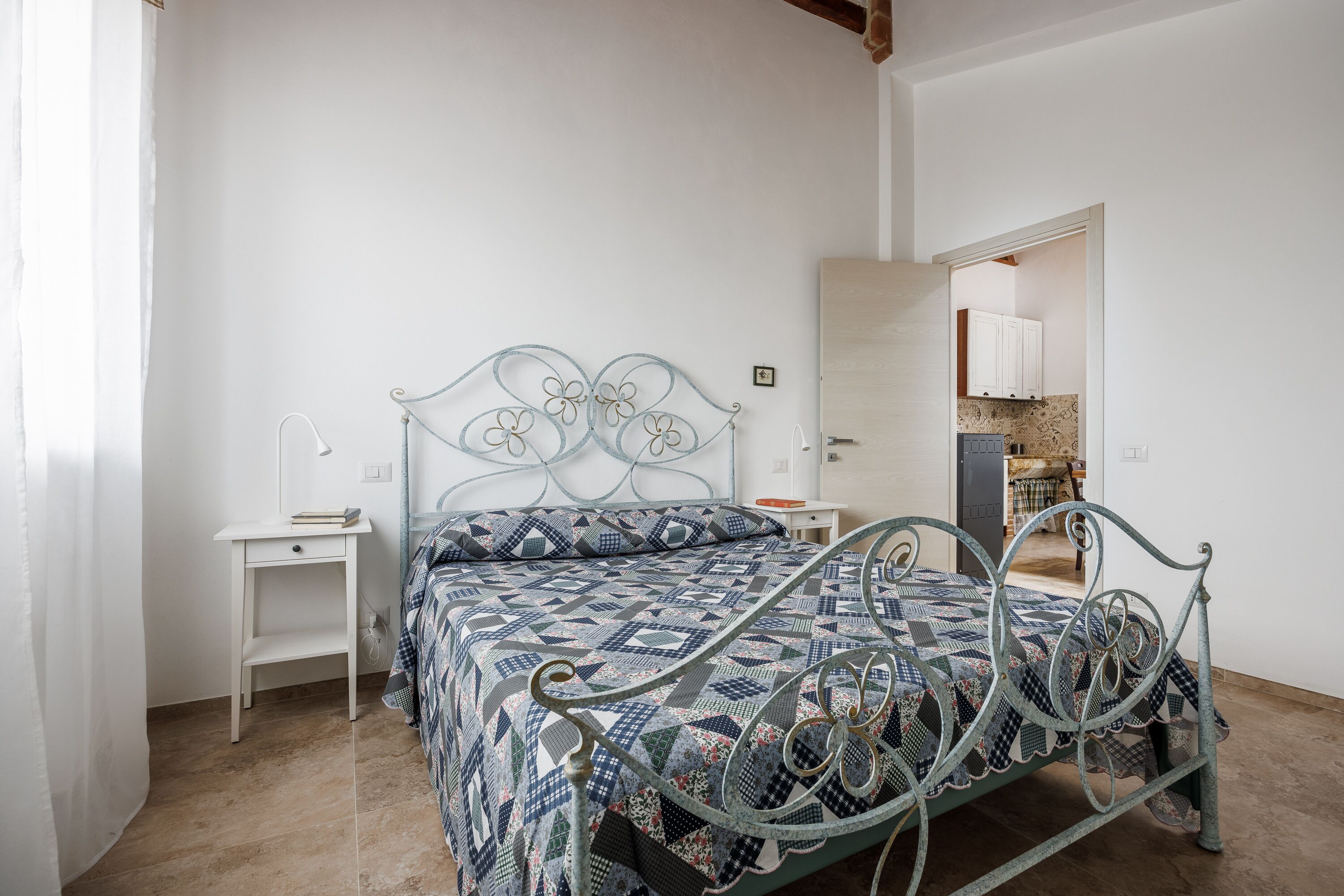 Un dormitorio con estructura de cama metálica, cubrecama estampado, mesita de noche y una pequeña mesa.