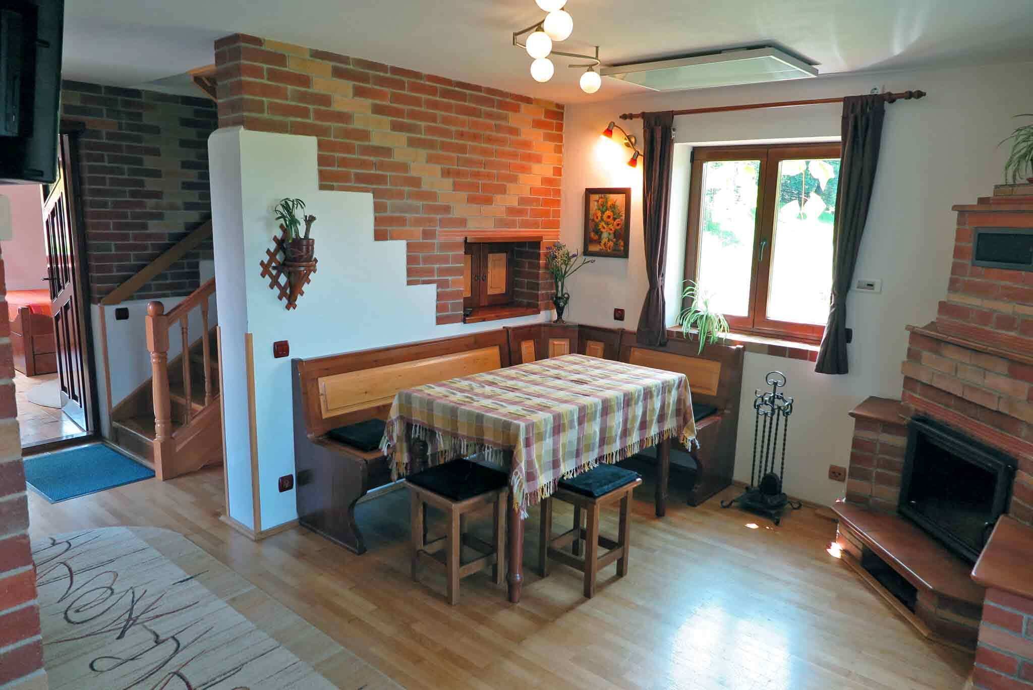 Un salon chaleureux avec une table en bois, des chaises, une cheminée et un escalier menant à un autre niveau.