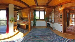 Una habitación amplia con techo de madera, un ventanal grande, una cama, un escritorio y una planta en maceta.