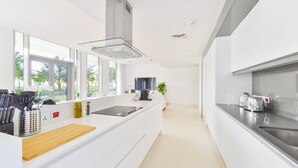 A modern kitchen with white cabinetry, a large island with a wooden countertop, and a view of the outdoors through large windows.