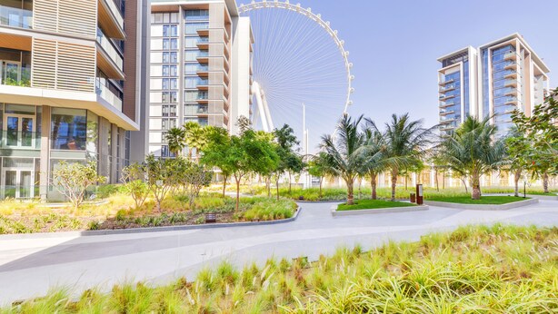 A modern building complex with a large Ferris wheel in the background, surrounded by landscaped areas and palm trees.