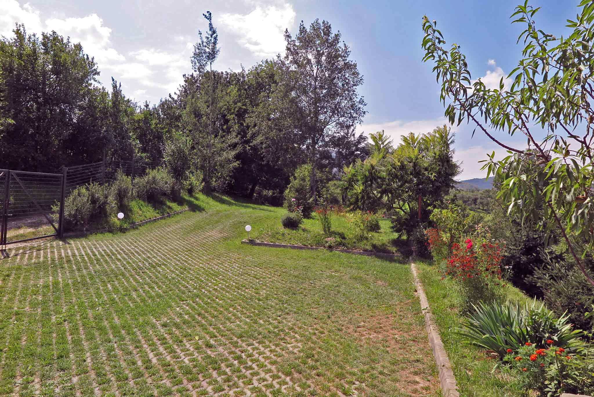 Ein gepflegter Garten mit befestigter Fläche, umgeben von verschiedenen Bäumen und Sträuchern.
