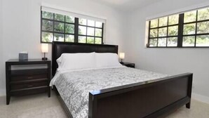A bedroom with a dark wooden bed, two bedside tables with lamps, and large windows with a view of greenery. - Cozy and Peaceful Home Near Beach (Pompano Beach)