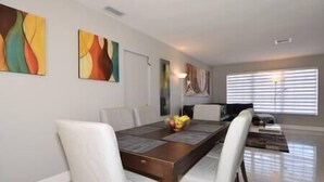 A dining area with a wooden table, white chairs, and abstract art on the walls. - Cozy and Peaceful Home Near Beach (Pompano Beach)