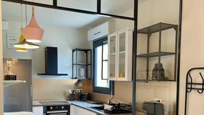 A compact kitchen with white cabinets, a black countertop, and a teal trash bin. - Les terrasses de valerian (Brignoles)