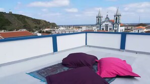 Terraza en la azotea con dos almohadas y una alfombra, con vistas a un pueblo costero y una iglesia destacada.