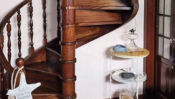 Una escalera en espiral de madera con pared blanca y suelo de baldosas.