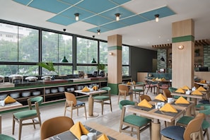 A modern restaurant with a long counter, multiple dining tables, and chairs. - MaxOneHotels Kota Harapan Indah Bekasi (Tarumajaya)
