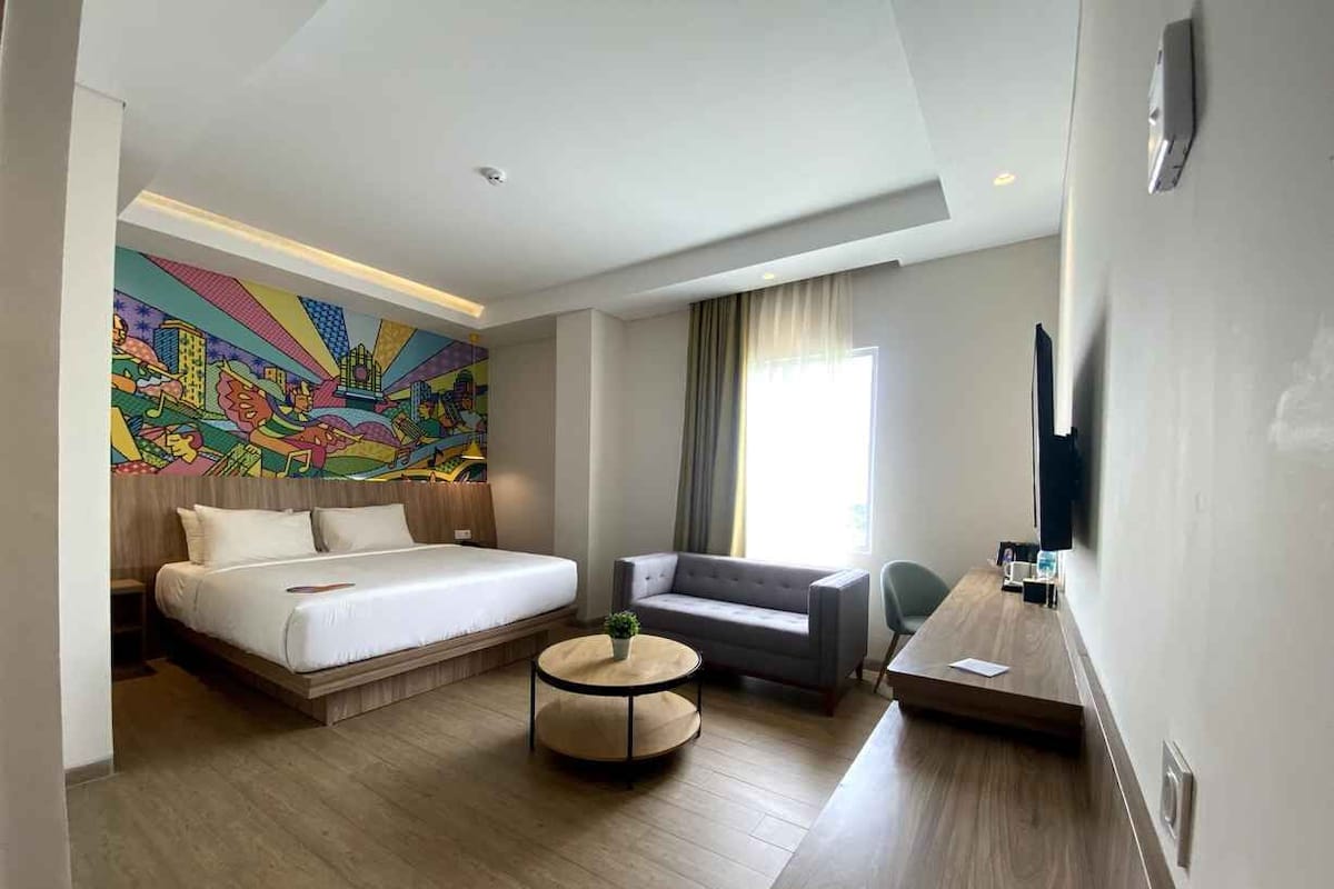 Une chambre d’hôtel avec un lit, un canapé, une table basse ronde et un téléviseur.