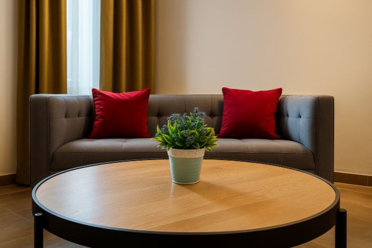 A modern living room with a grey sofa, two red cushions, and a round wooden coffee table with a green plant.