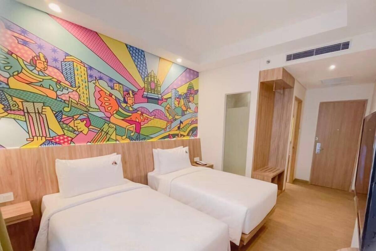 Une chambre d’hôtel avec deux lits, une fresque murale aux couleurs vives et un plancher en bois.