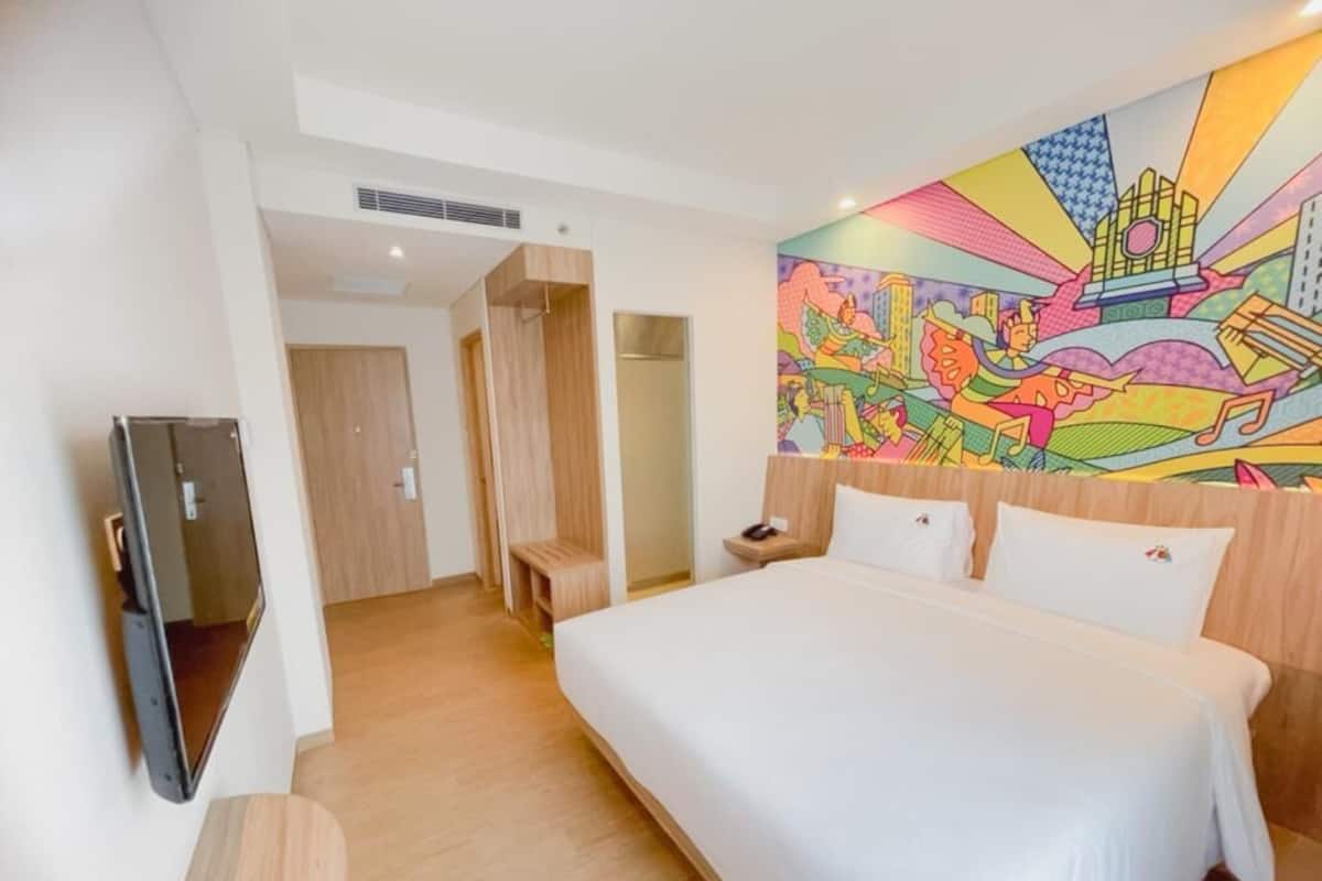 Une chambre d’hôtel avec un grand lit, une télévision et une fresque murale aux couleurs vives.