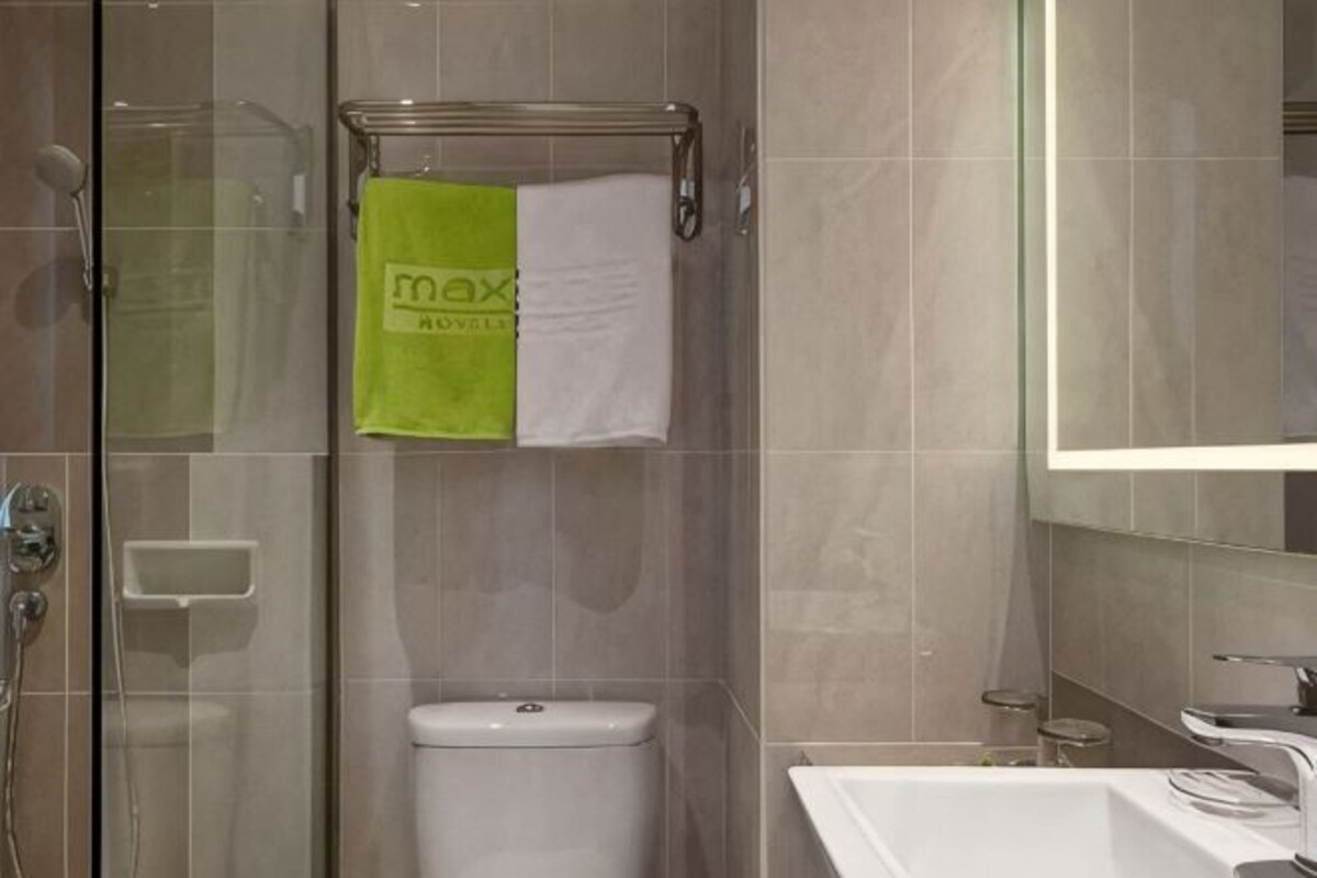 A bathroom with a glass shower enclosure, a toilet, a sink, and a towel rack with a green and white towel.