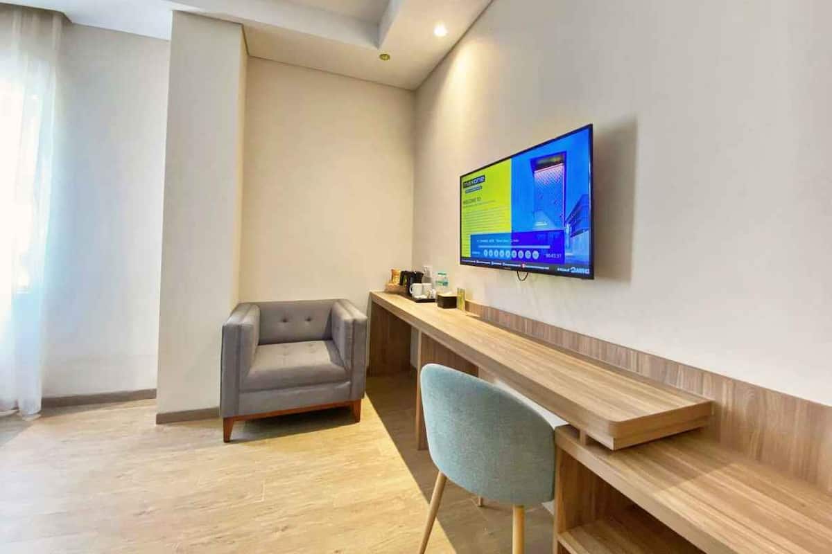 Une chambre d’hôtel moderne avec un canapé gris, un bureau en bois et un téléviseur à écran plat fixé au mur.