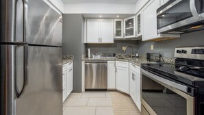 A modern kitchen with stainless steel appliances, white cabinetry, and a granite countertop. - Two Bedroom Townhome On Canal! (Ocean City)