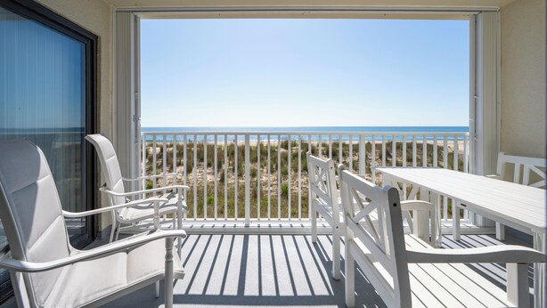 A balcony with a white table and chairs, overlooking a beach with a fence. - Oceanfront 2 bedroom in desirable North OC (Ocean City)