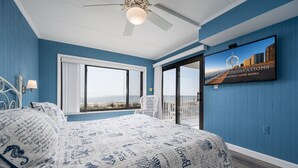 A bedroom with a large bed, a ceiling fan, a TV on the wall, and a balcony with a view. - Oceanfront 2 bedroom in desirable North OC (Ocean City)