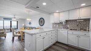 A modern kitchen with white cabinetry, a large island, and a dining area with a view. - Oceanfront 2 bedroom in desirable North OC (Ocean City)