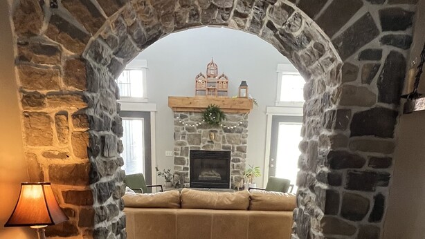 A stone archway leading to a living room with a fireplace, sofa, and a lamp on a side table. - Luxury Mountain Retreat Near Midway & Park City – Sleeps 10 (Heber City)